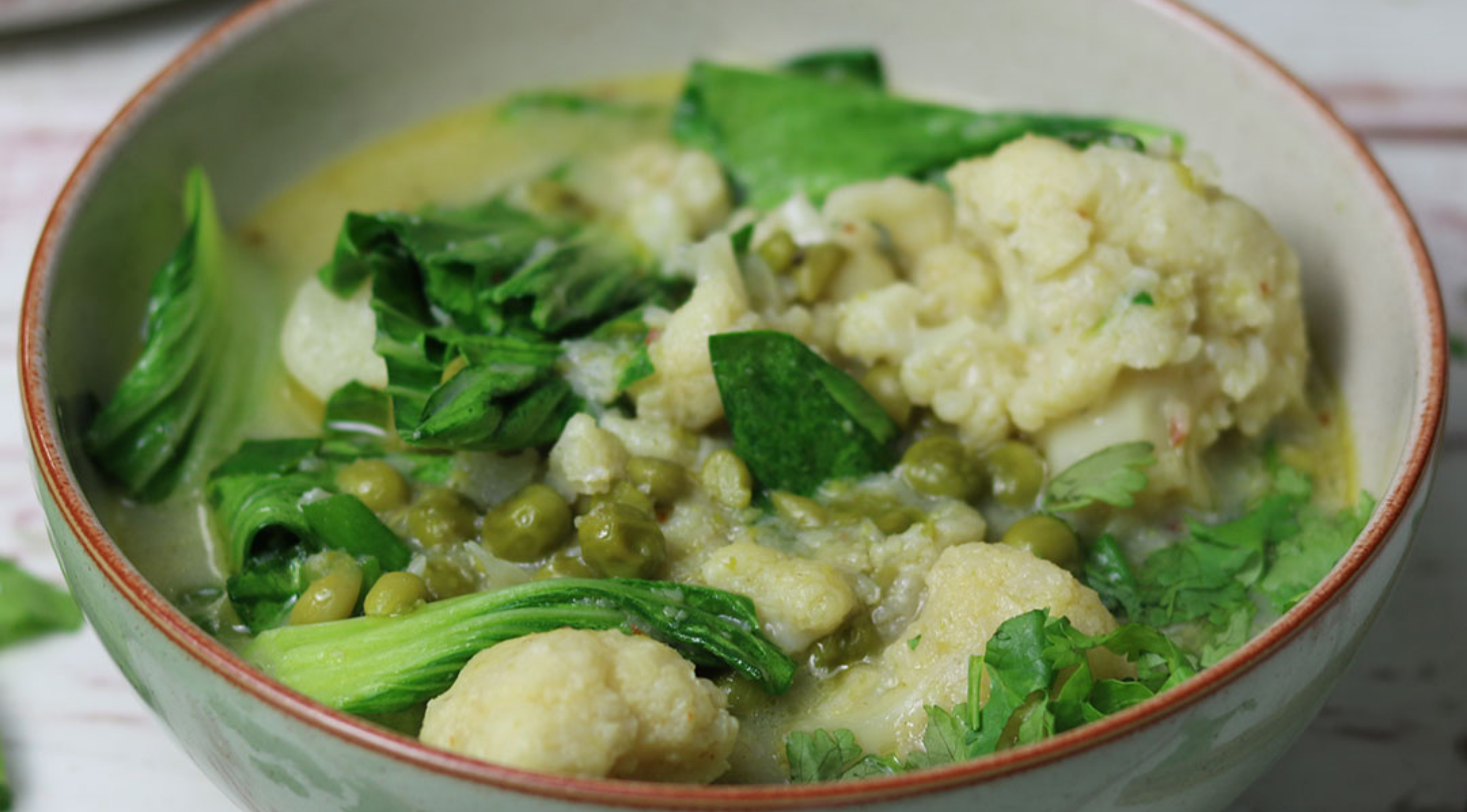 Eine Schüssel Gemüsecurry mit Blumenkohl, Erbsen, Bok Choy und Koriander in leichter grüner Soße, serviert mit Fissler Kochgeschirr.