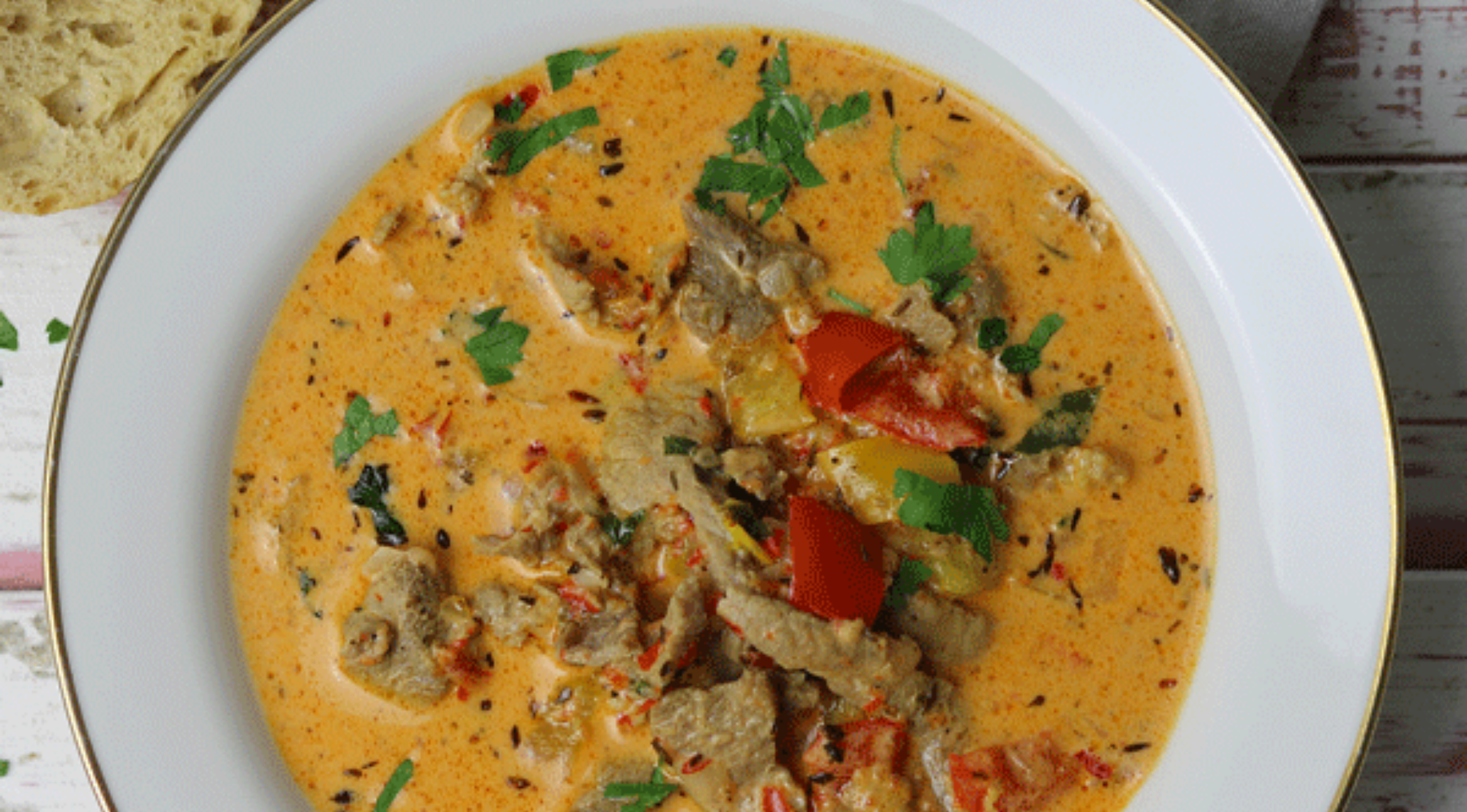 Ein deftiger Eintopf mit Fleisch und Paprika, garniert mit Petersilie auf einem eleganten weißen Teller - bereiten Sie Ihre Mahlzeit mit dem Präzisionskochgeschirr von Fissler zu.