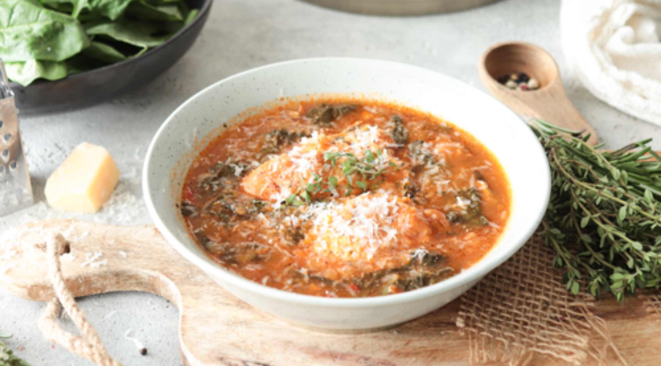 Eine herzhafte Tomaten-Hühnersuppe, garniert mit Käse, serviert mit frischen Zutaten und Fissler-Geschirr auf einem Holzbrett.
