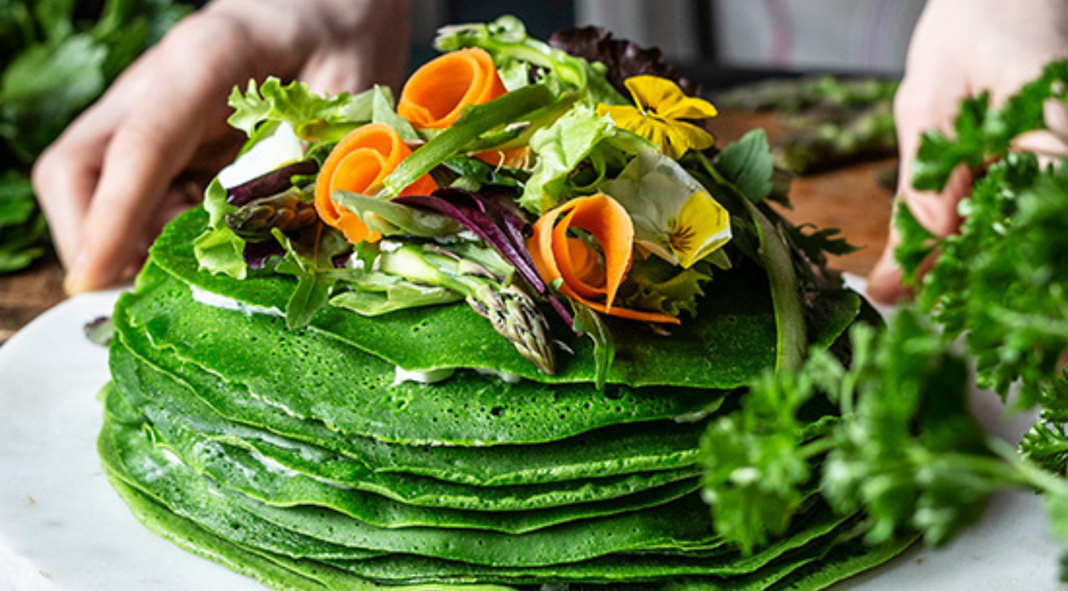 Ein frischer Stapel grüner Pfannkuchen mit knackigem Gemüse und essbaren Blumen, perfekt angerichtet mit Fissler Kochgeschirr - deutsche Qualität, zeitloses Design.