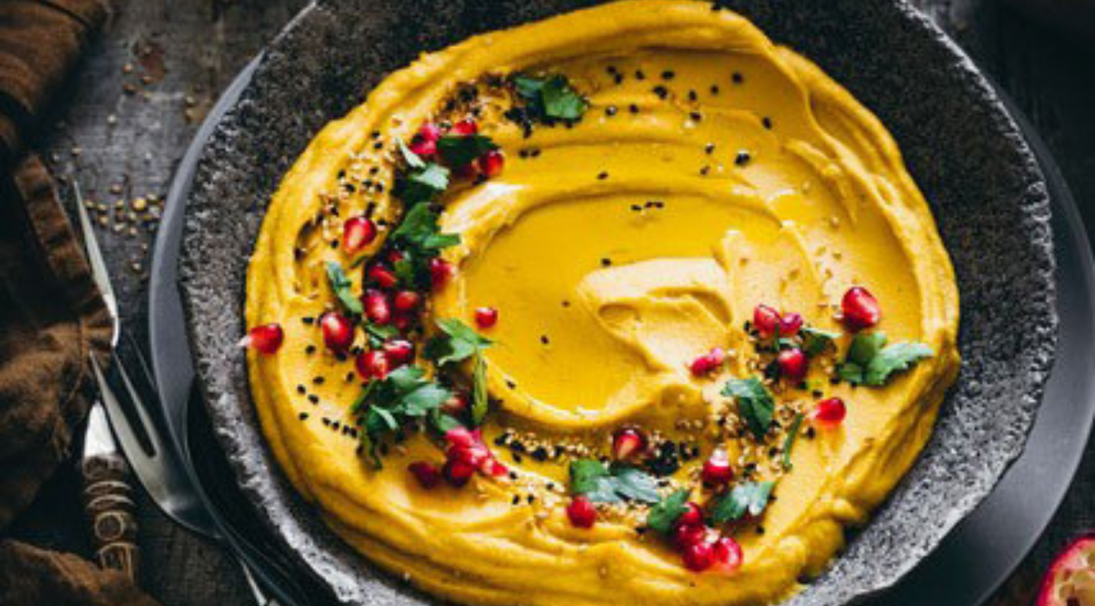 Eleganter Hummus mit lebhaften Toppings in einer eleganten dunklen Schale, präsentiert auf einer rustikalen Oberfläche - die perfekte Lösung für Ihre Fissler-Küche.