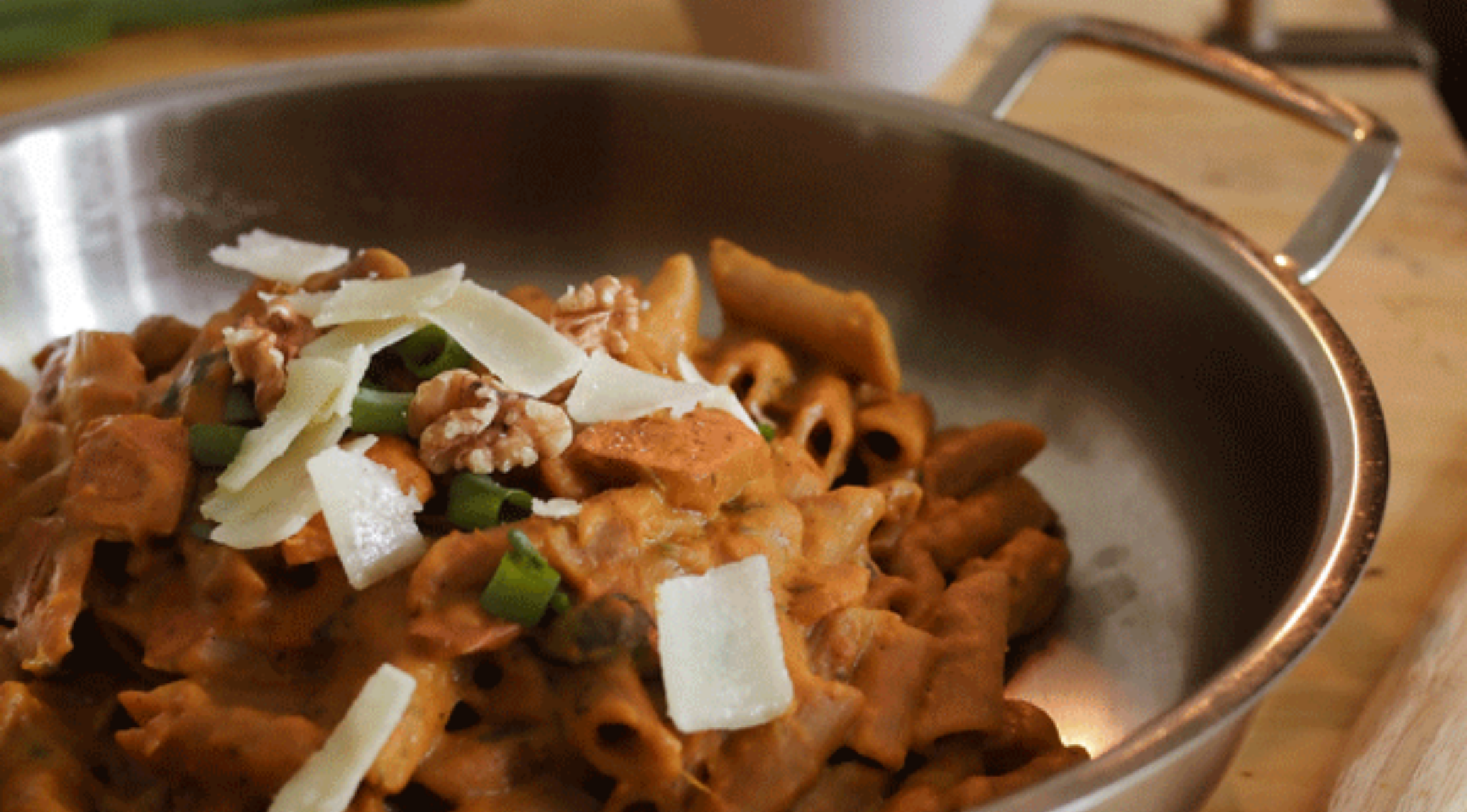 Cremige Pasta mit Parmesan, Walnüssen und grünen Zwiebeln in einer hochwertigen Fissler-Edelstahlschale auf einem Holztisch.