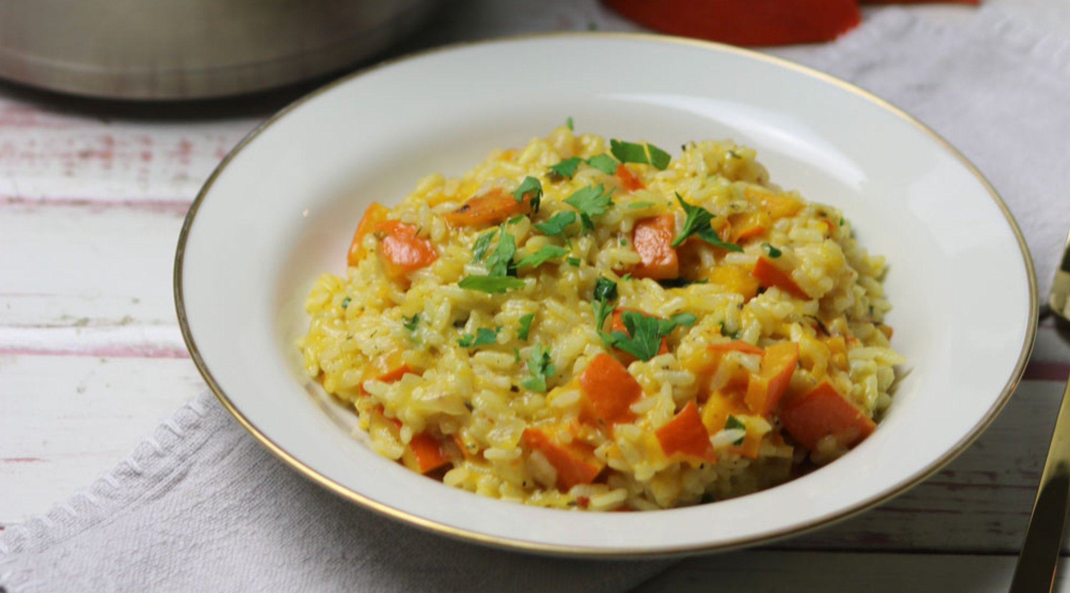 Ein goldumrandeter Teller mit cremigem Risotto mit Paprika und Kräutern, präsentiert auf einer weißen Oberfläche - perfekt zubereitet mit Fissler-Kochgeschirr.