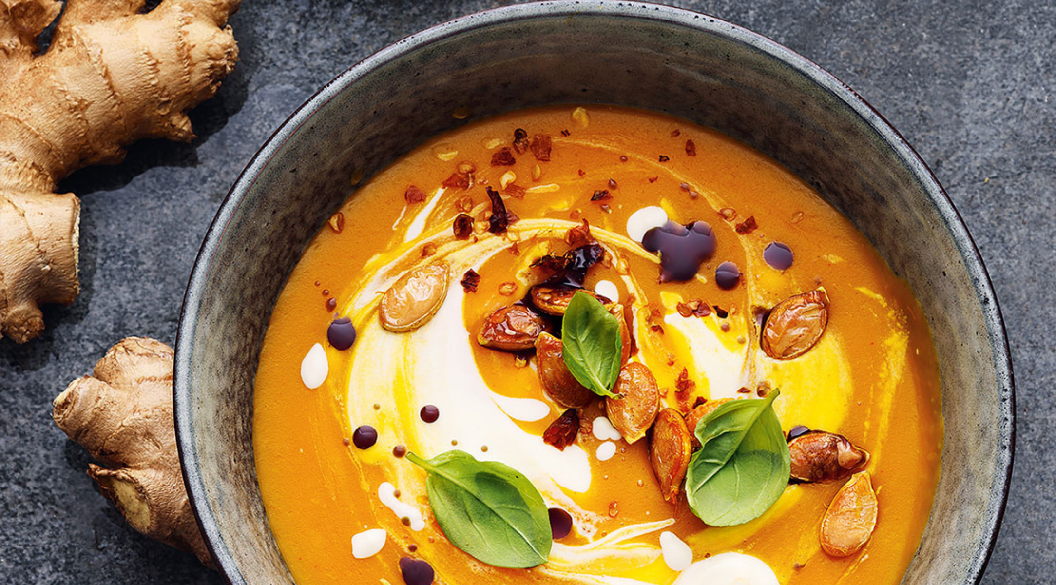 Cremige Orangensuppe mit Gourmet-Garnituren in einer Fissler-Schale, neben Ingwer, auf einer elegant dunklen Oberfläche - zeitloses deutsches Design.