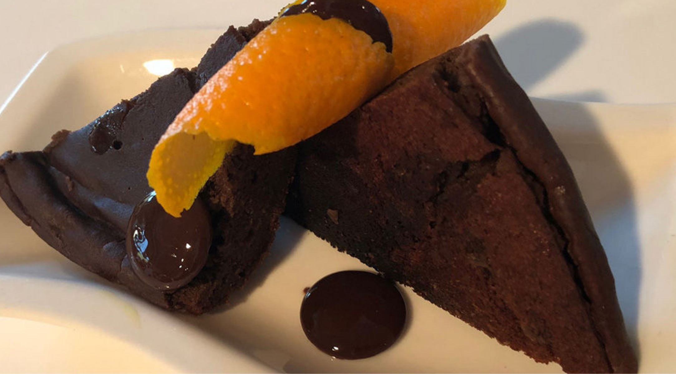 Zwei Scheiben Schokoladenkuchen mit Orangenschale und Schokoladenspritzern, kunstvoll präsentiert auf einem von Fissler gefertigten weißen Teller.