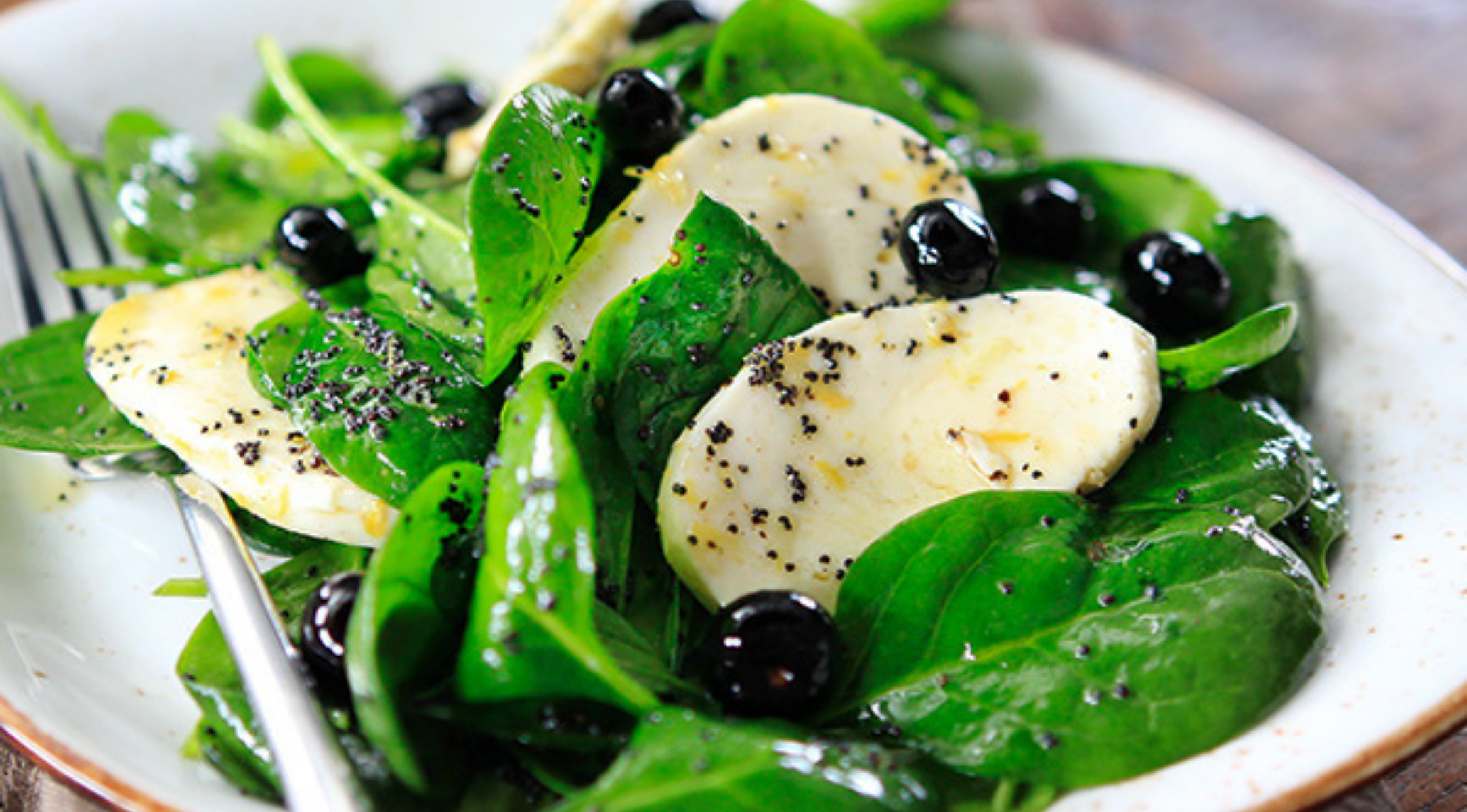 Frischer Spinatsalat mit Mozzarella, Blaubeeren und schwarzem Pfeffer auf einem weißen Teller, elegant serviert mit Fissler-Besteck.