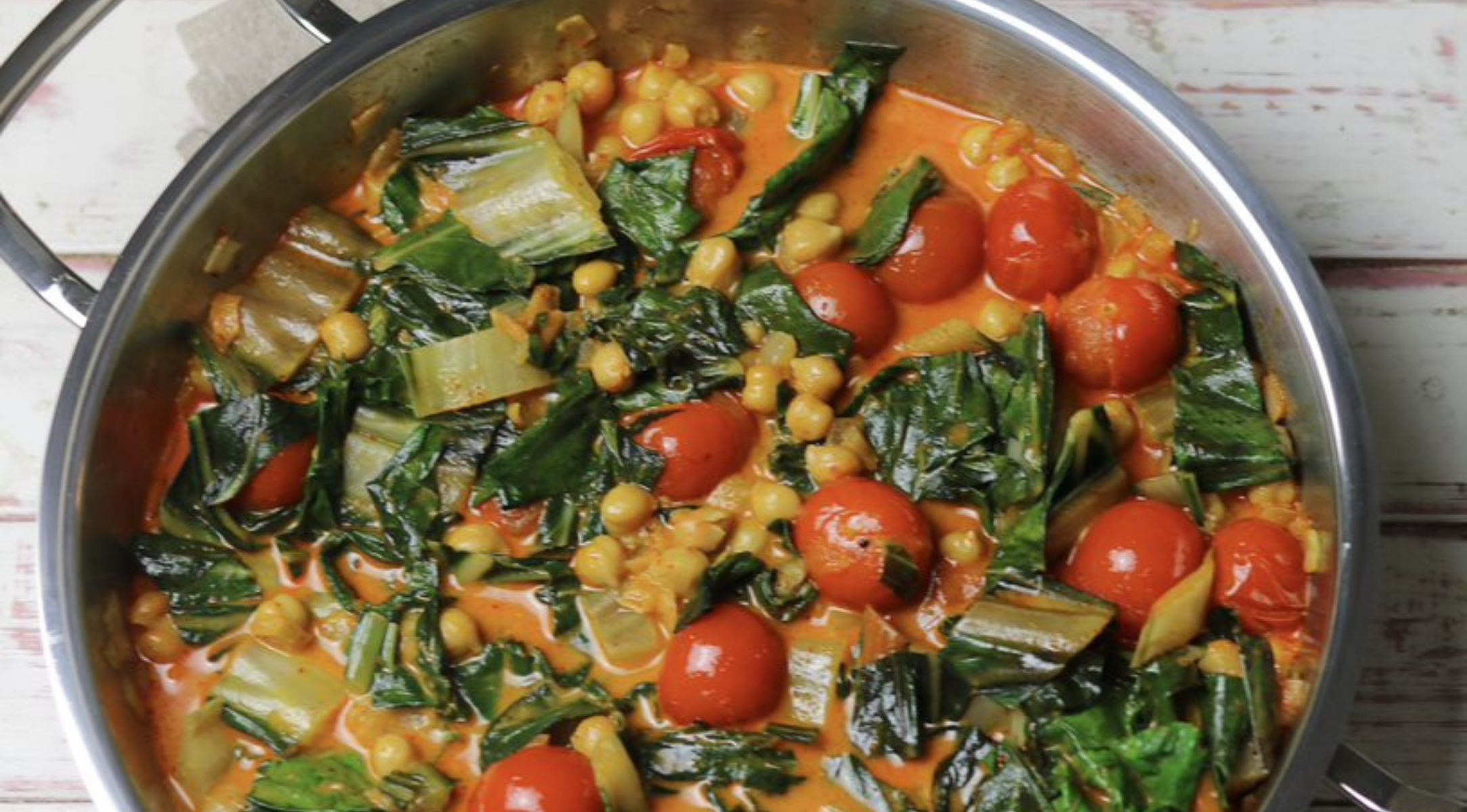 Eine Fissler-Edelstahlpfanne, gefüllt mit lebhaftem Curry, die unser deutsches Präzisionskochgeschirr auf einer rustikalen weißen Oberfläche zur Geltung bringt.