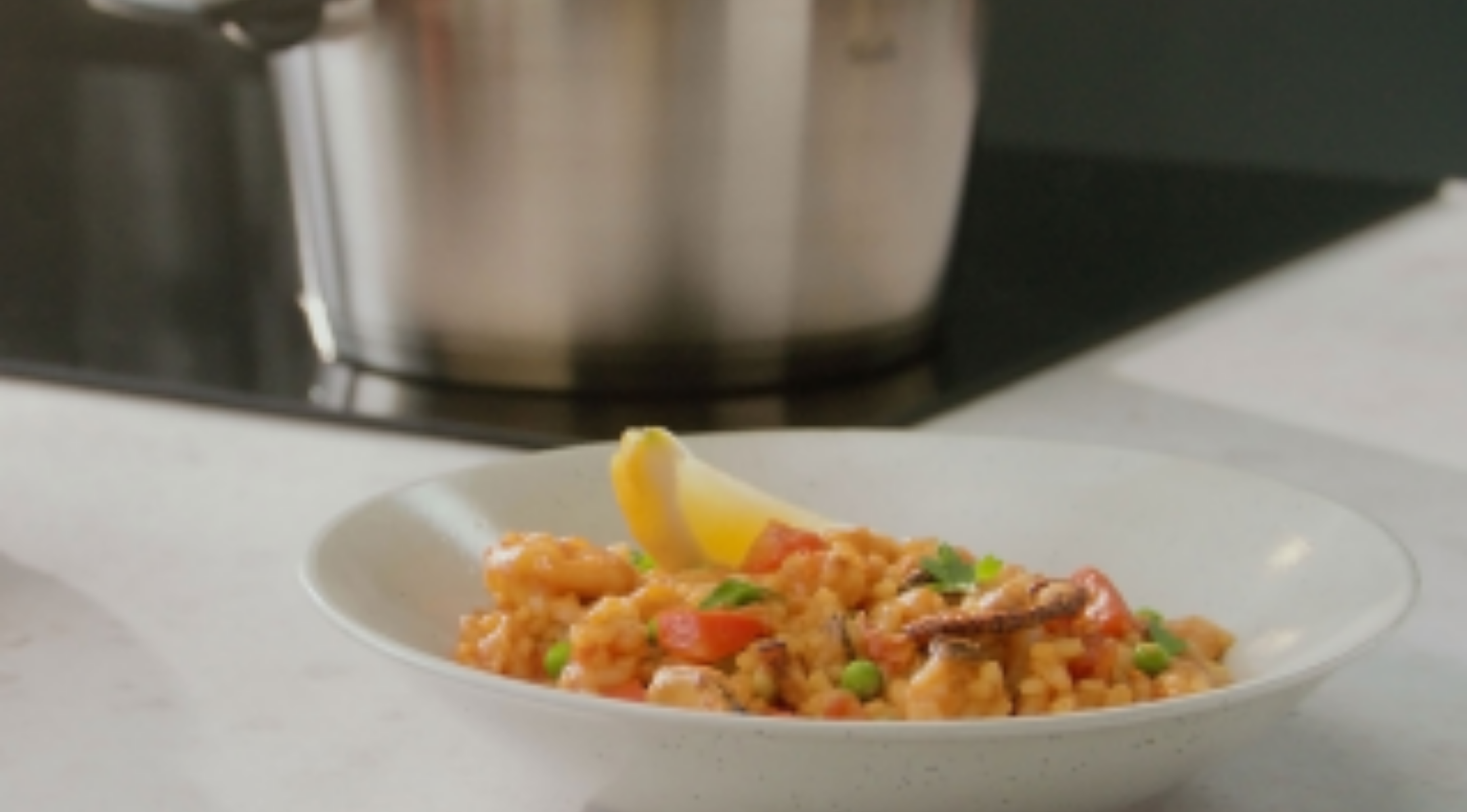 Ein lebhaftes Reisgericht mit Garnelen und Gemüse, serviert neben einem hochwertigen Fissler-Edelstahltopf, der in Deutschland hergestellt wird.