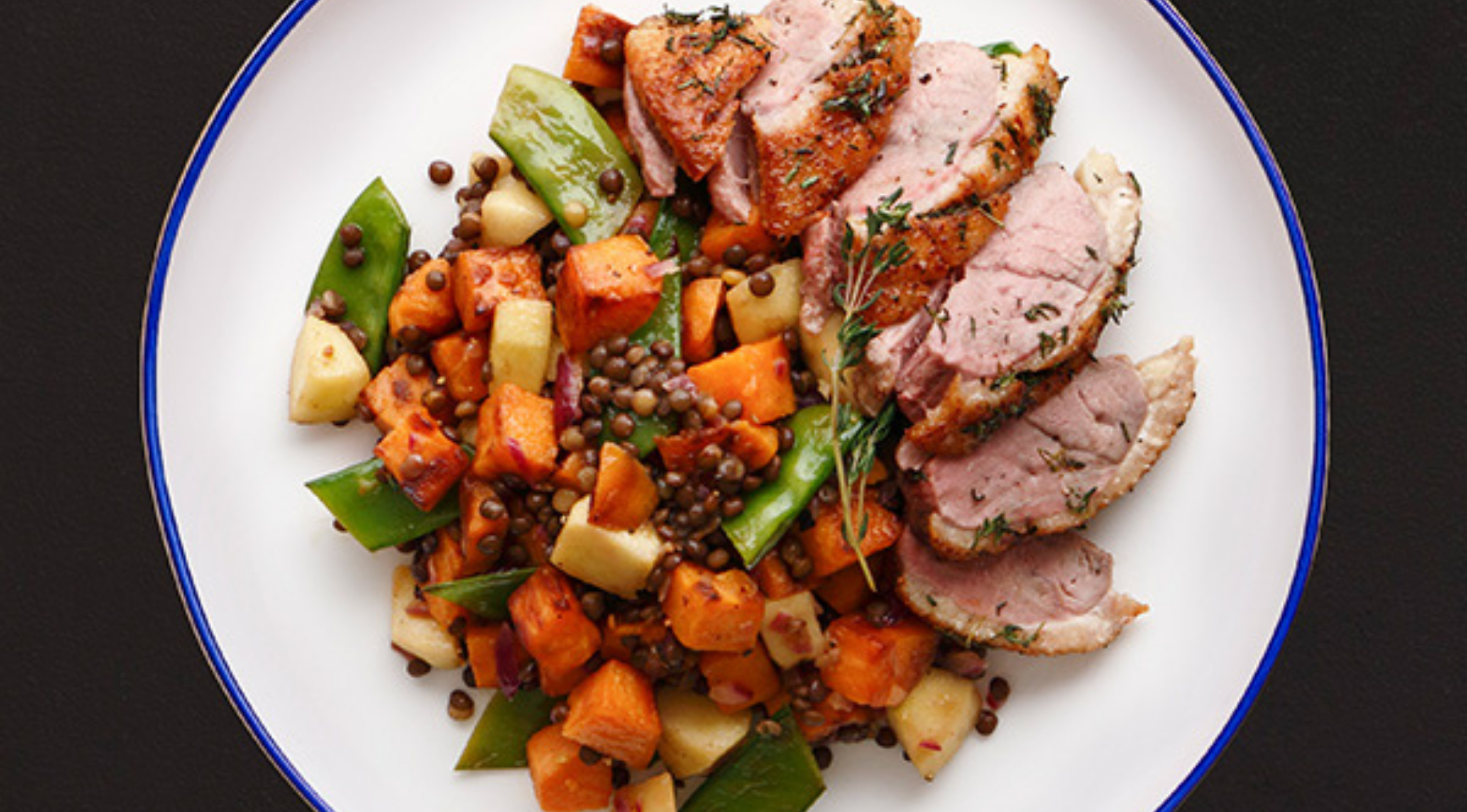 Elegant gebratenes Schweinefilet mit Linsen, Süßkartoffeln, Zuckererbsen und Äpfeln auf feinem Geschirr - präzise gegart in Fissler-Qualität.