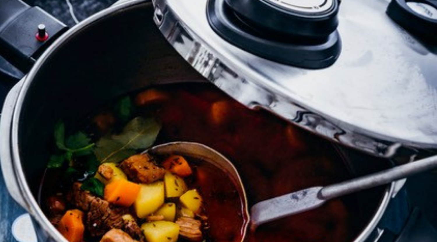 Ein Schnellkochtopf von Fissler aus Edelstahl lässt Dampf ab, während eine Schöpfkelle einen reichhaltigen Eintopf aufhebt, und unterstreicht damit deutsche Präzision und Langlebigkeit.
