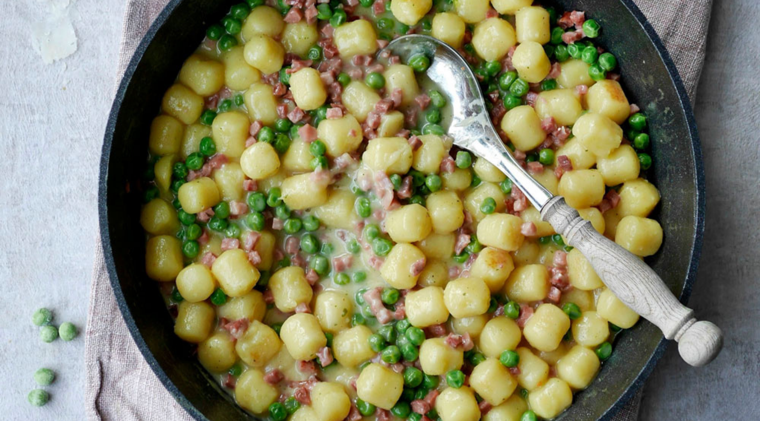 Eine Fissler-Pfanne mit cremigen Gnocchi, Erbsen und Schinkenwürfeln, die deutsche Präzisionsarbeit und zeitloses Design unterstreicht.