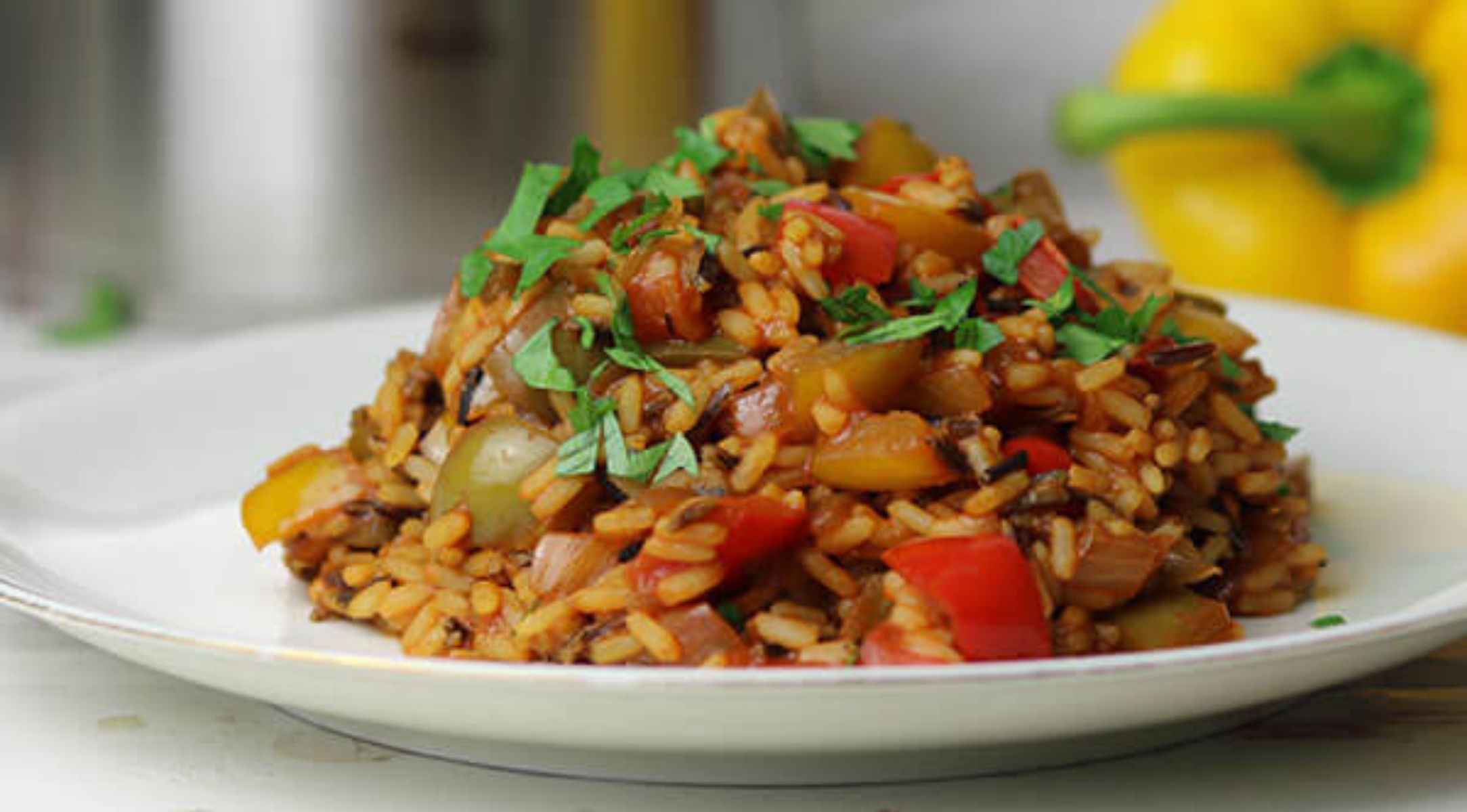 Bunter Gemüsereis mit Paprika und Kräutern auf einem weißen Teller, zubereitet mit Fissler-Kochgeschirr. Gelbe Paprika verschwommen dahinter.