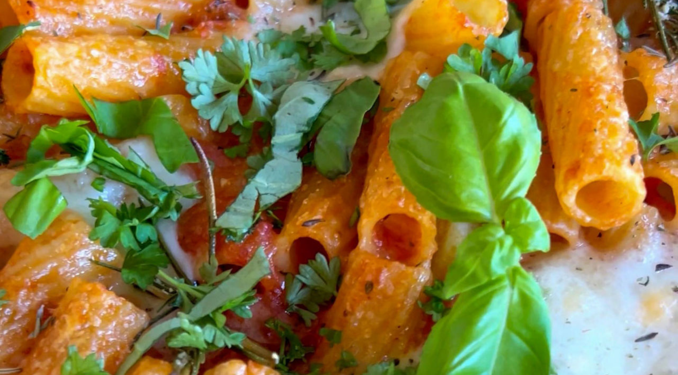 Überbackene Rigatoni mit Tomatensauce und Käse, verfeinert mit Basilikum und Petersilie, zubereitet in einer hochwertigen Fissler-Edelstahlpfanne.