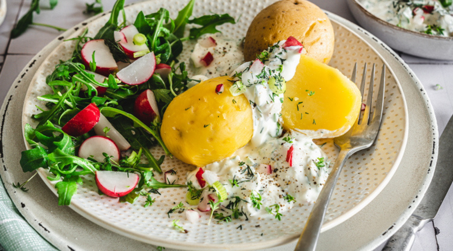 Salzkartoffeln mit Kräuterrahmsauce, Salat und Brötchen, elegant serviert mit einer Fissler-Edelstahlgabel.