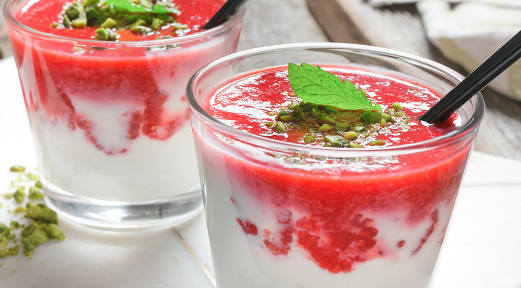 Zwei Gläser Joghurt mit Fruchtpüree und Pistazien, elegant präsentiert - Perfektion wird mit Fissler Küchengeräten zum Kinderspiel.