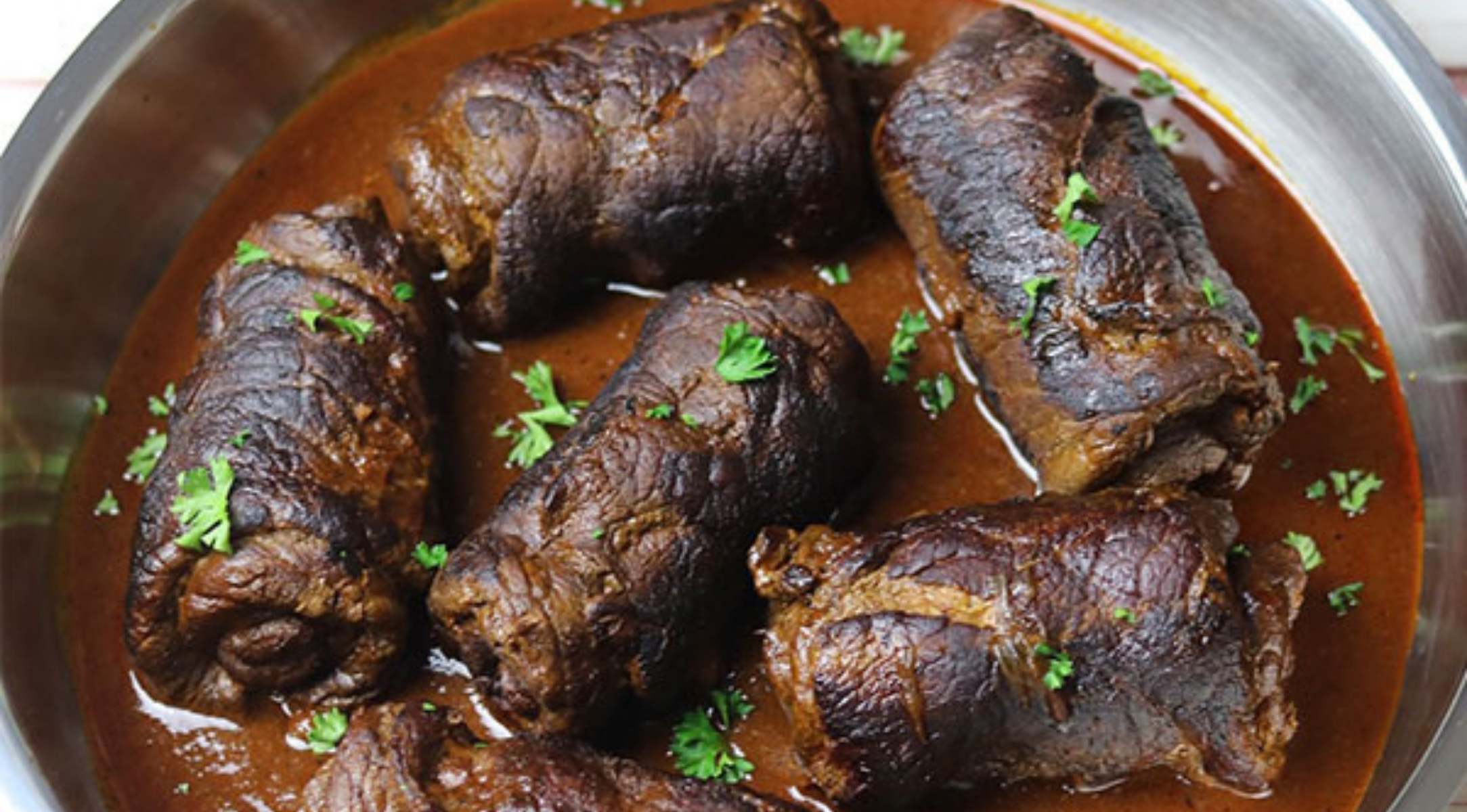 Geschmorte Rinderrouladen in reichhaltiger Sauce, garniert mit Petersilie, elegant serviert in einer Fissler-Edelstahlpfanne.