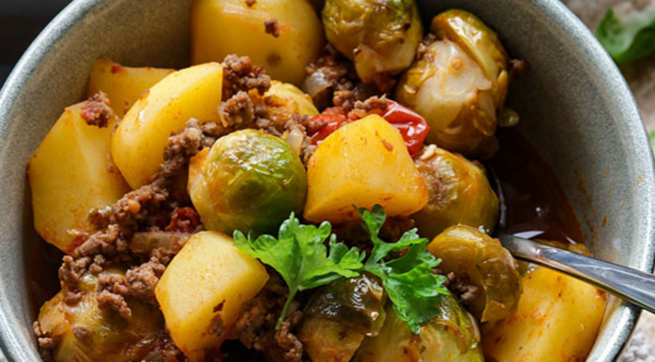 Herzhafter Eintopf mit Kartoffeln, Rosenkohl, Rindfleisch und Tomaten, serviert in einer Schüssel - perfekt zubereitet im Fissler Kochgeschirr.