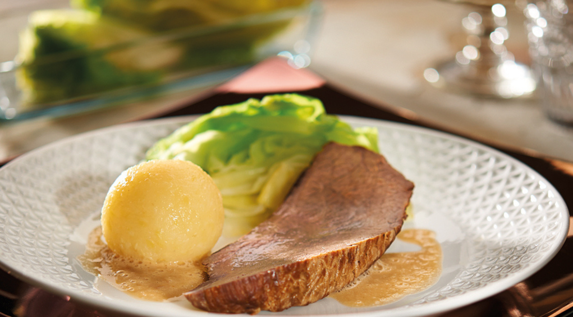 Ein klassisches deutsches Gericht mit Rinderbraten in Bratensoße, Kartoffelknödel und gedünstetem Kraut, kunstvoll serviert auf einem fein gearbeiteten Teller.