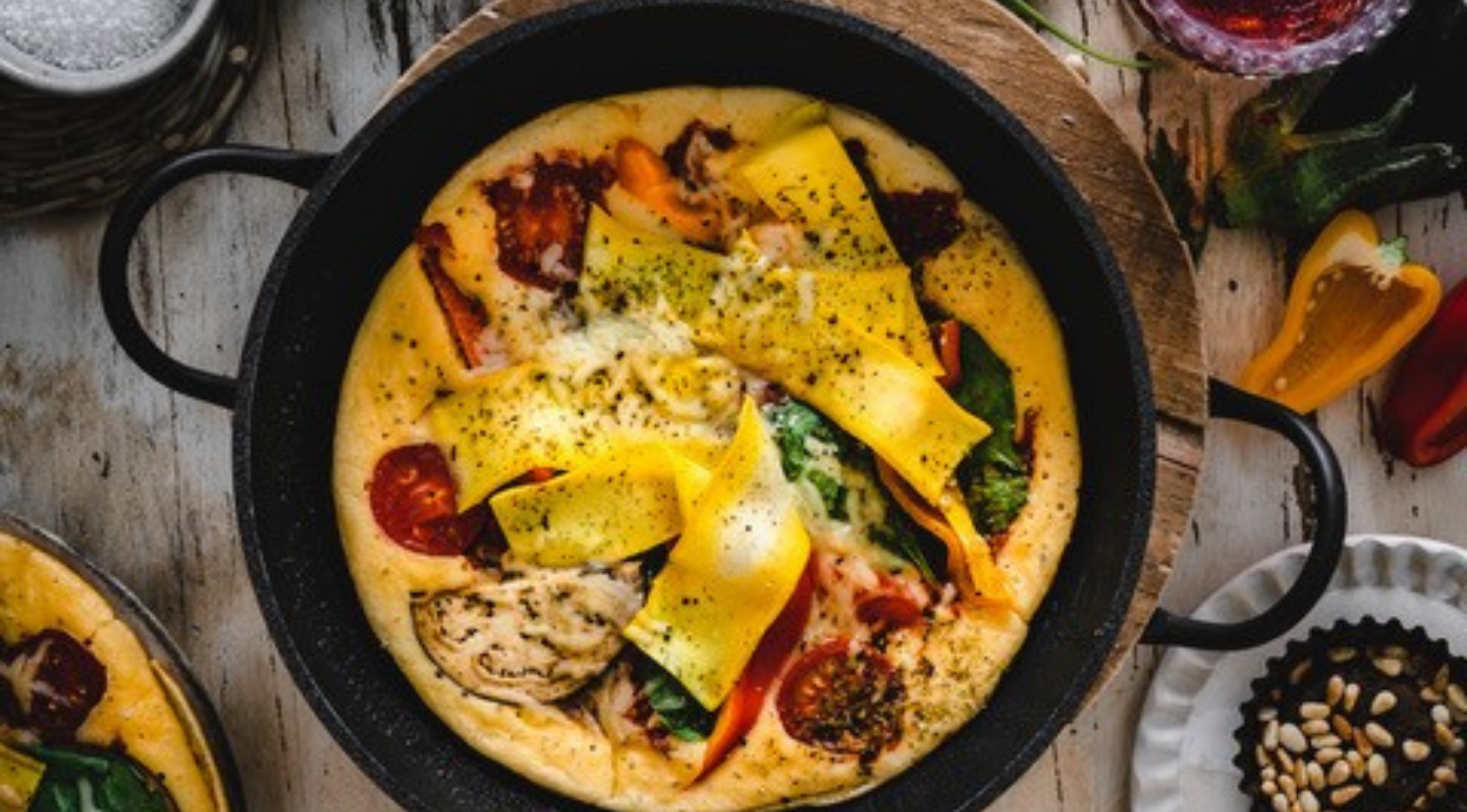 Eine lebendige Frittata in einer hochwertigen Fissler-Pfanne, überbacken mit Käse und Gemüse, präsentiert auf einem rustikalen Tisch mit frischen Zutaten.