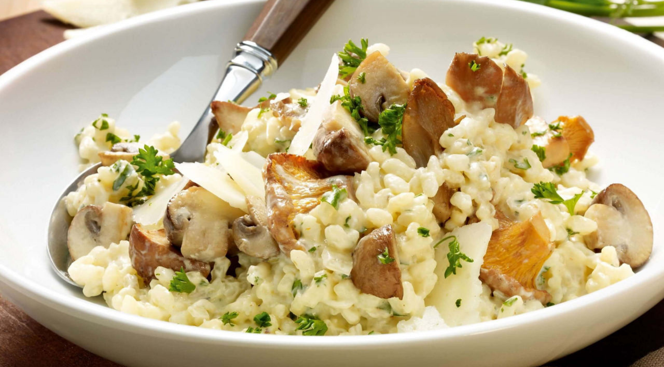 Cremiges Risotto mit Petersilie, Pilzen und Parmesan, serviert in einer Fissler-Edelstahlschale mit elegantem Löffel und Gabel.