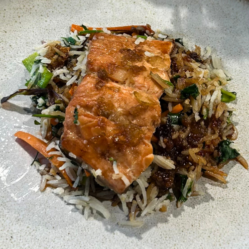 Perfekt gebratener Lachs auf gebratenem Gemüsereis, kunstvoll angerichtet - ein Beweis für die zeitlose Präzision und Qualität von Fissler Kochgeschirr.