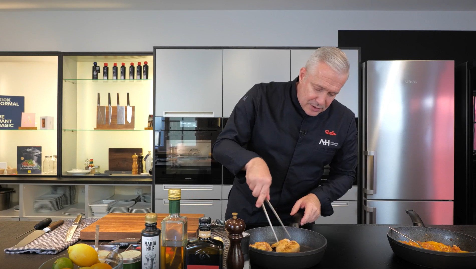 Ein Koch kocht in einer modernen Küche mit Fissler-Kochgeschirr aus rostfreiem Stahl. Die Zutaten und Gewürze liegen auf der Theke daneben.