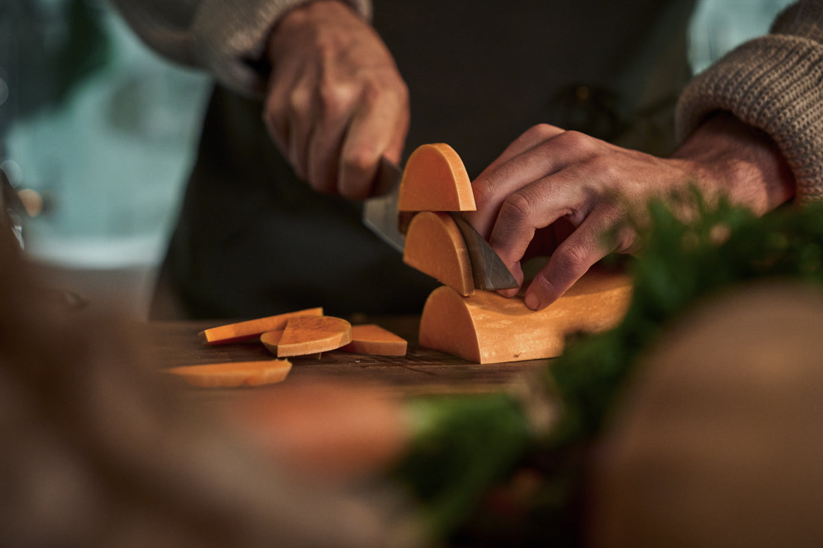 A person prepares a butternut squash with precise knife work on a wooden surface, surrounded by fresh produce and hints of greenery in the foreground. The scene reflects Fissler’s commitment to timeless design and innovation in the kitchen, where durable cookware and expertly engineered kitchen tools ensure exceptional culinary results.