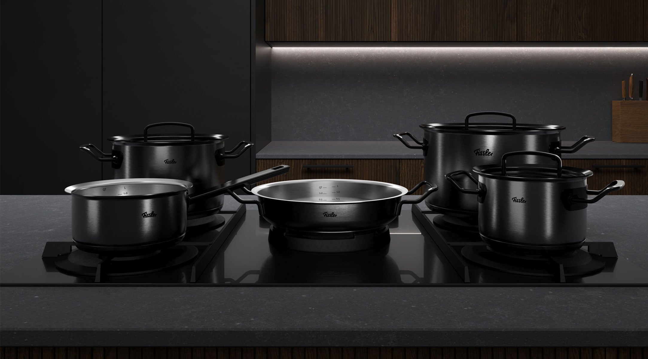 Fissler Kochgeschirrset: fünf hochwertige schwarze Töpfe und Pfannen mit Deckeln auf einer eleganten Herdplatte, die zeitloses deutsches Design zeigt.