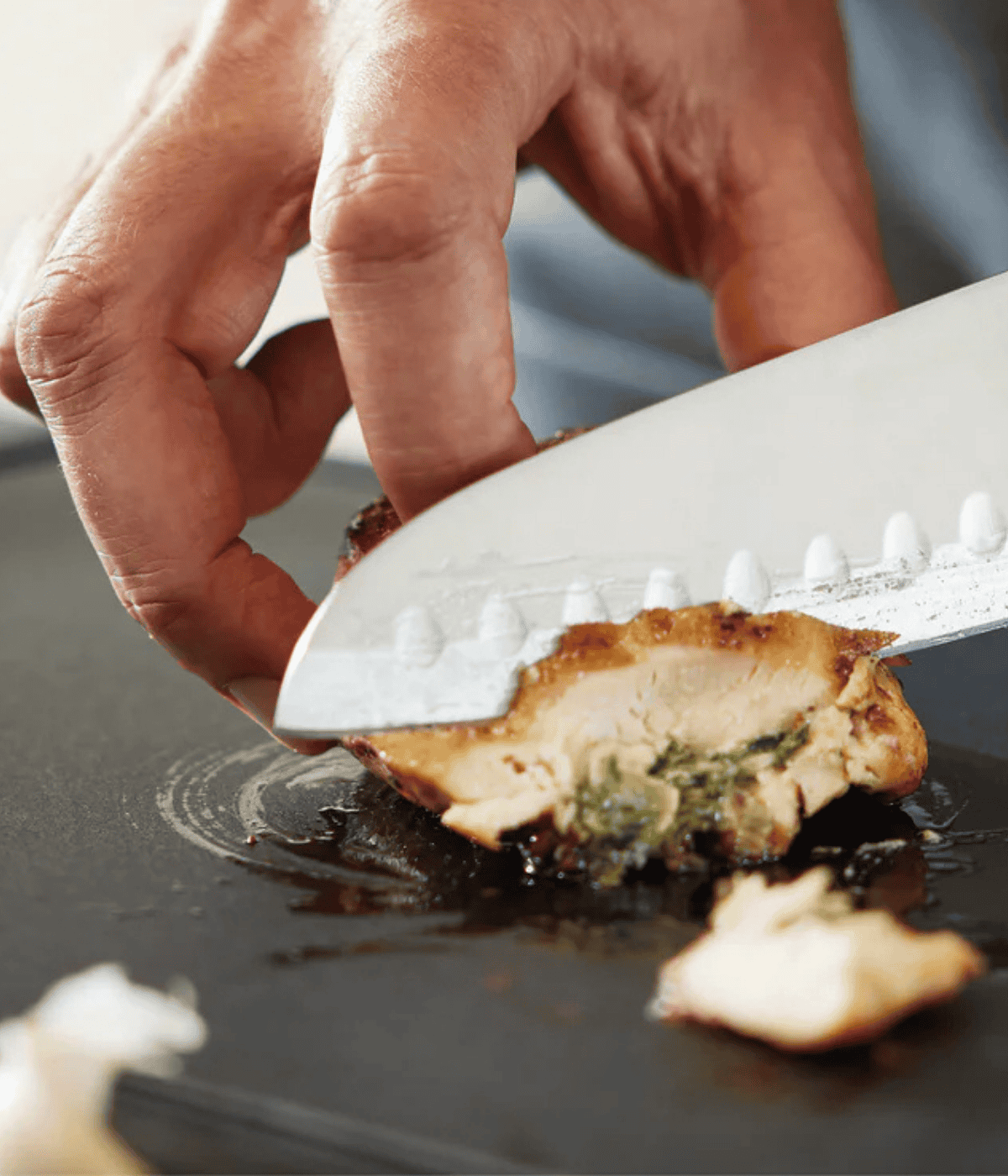 Eine Hand schneidet auf einem Schneidebrett mit einem Fissler-Kochmesser fachmännisch gefüllte Hähnchen in Scheiben und stellt damit Präzision und hochwertiges Kochgeschirr unter Beweis.