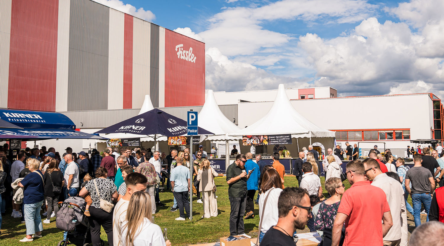 Neben dem ikonischen Fissler-Gebäude genießen die Besucher Gourmet-Essen und entdecken unter sonnigen Zelten und Schirmen hochwertige deutsche Kochgeräte.