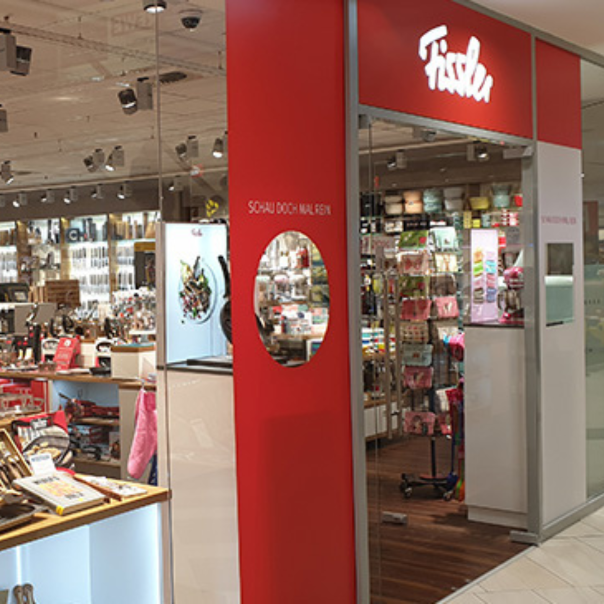 Fissler-Schaufenster mit dem charakteristischen rot-weißen Schild, Glasfassade und hochwertigem deutschen Kochgeschirr - Töpfe, Pfannen und Zubehör - in der Auslage.