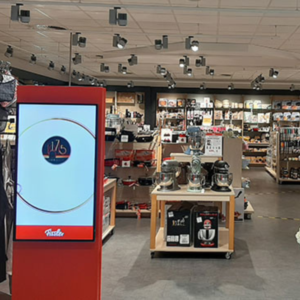 Fissler-Laden mit Regalen mit hochwertigen Töpfen, Pfannen und Kochgeschirr aus deutscher Produktion. Digitaler "175"-Bildschirm am Eingang. Hell, organisiert.