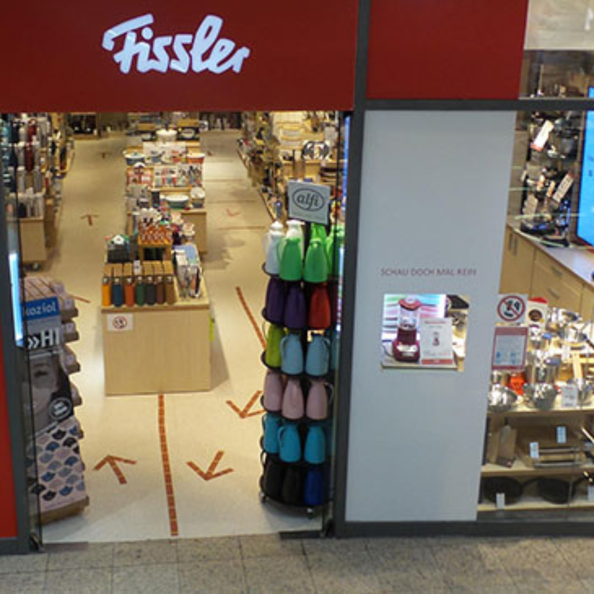Die Fissler-Schaufensterfront mit dem ikonischen roten Schild, die Wasserkocher am Eingang und die Regale mit hochwertigem deutschen Kochgeschirr leiten die Kunden ins Innere.