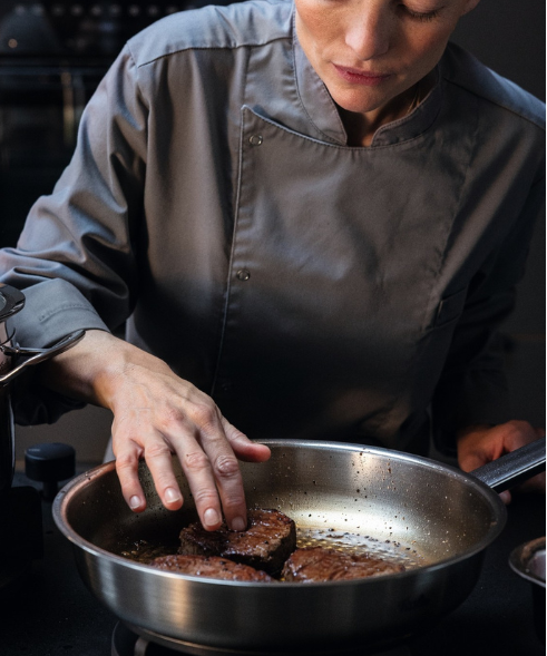 In einer modernen Küche bereitet ein Chefkoch in Grau mit einer Fissler-Edelstahlpfanne fachmännisch und präzise Fleischpasteten zu.