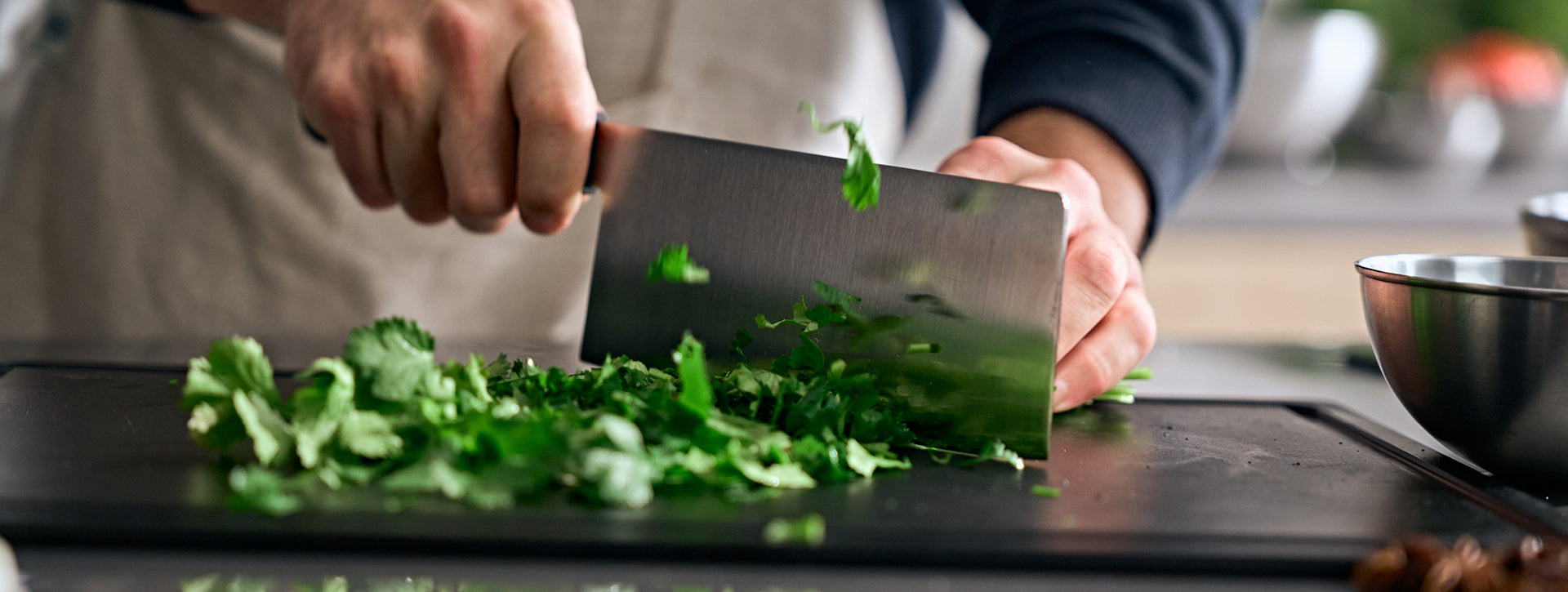 Eine Person schneidet frische grüne Kräuter mit einem hochwertigen Fissler-Messer auf einem schwarzen Schneidebrett, das deutsche Qualität und Präzision widerspiegelt.