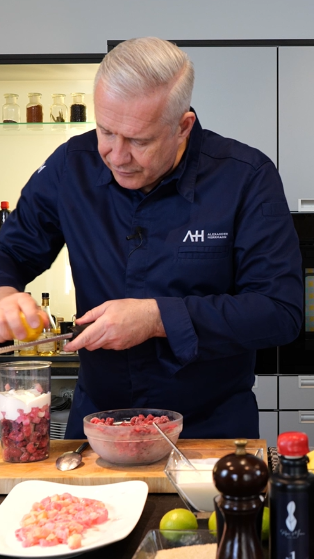 A chef grates lemon zest over meat and onions on a wooden countertop, using high-quality Fissler cookware in an elegant, modern kitchen.