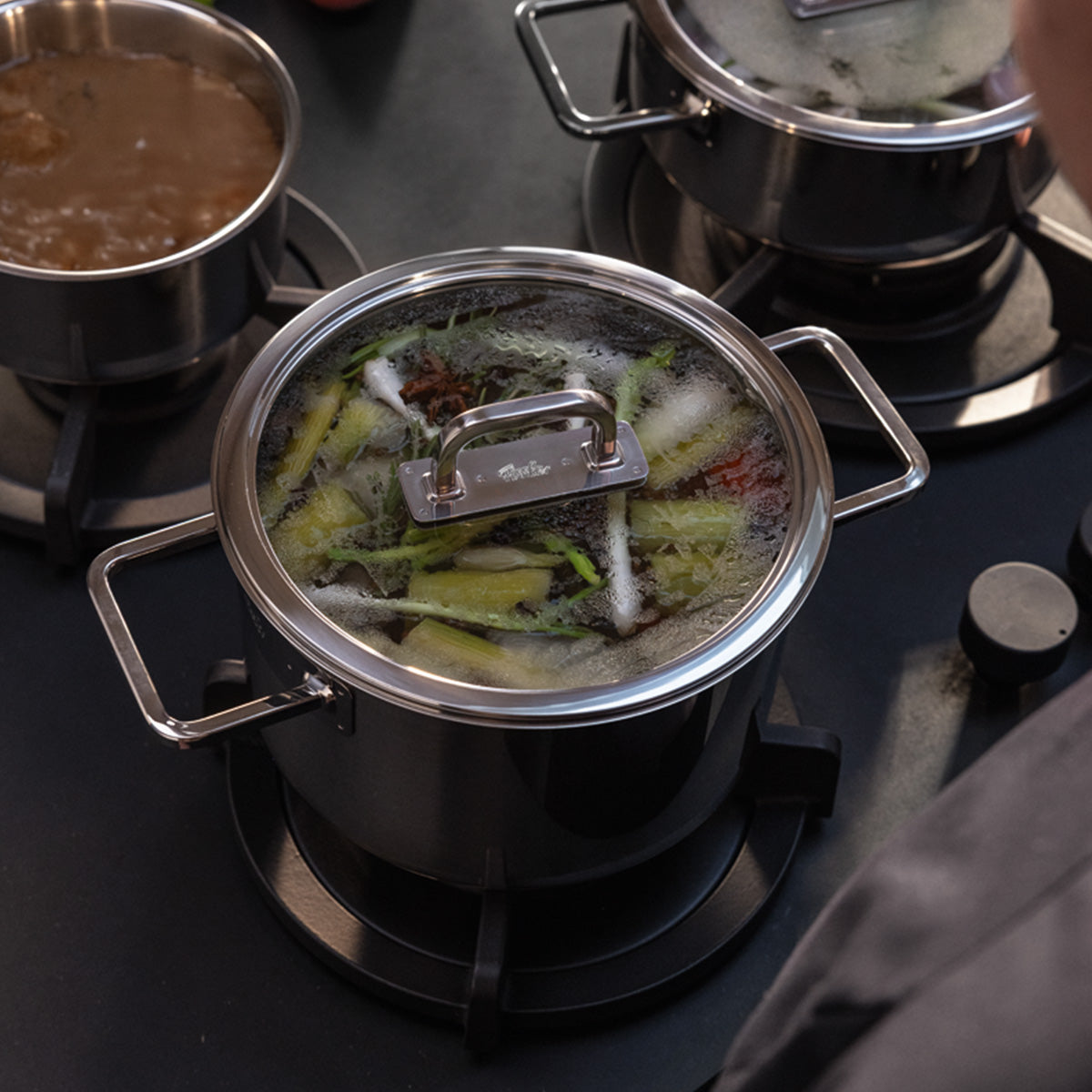 Der Fissler Viseo® Pro 20 cm Topf mit Glasdeckel köchelt auf dem Herd; andere Fissler Kochgeschirre und Stielkasserolle begleiten ihn.
