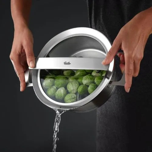 Eine Köchin gießt den Rosenkohl aus einem Fissler-Edelstahltopf ab, indem sie den integrierten Siebdeckel mit beiden Händen benutzt.