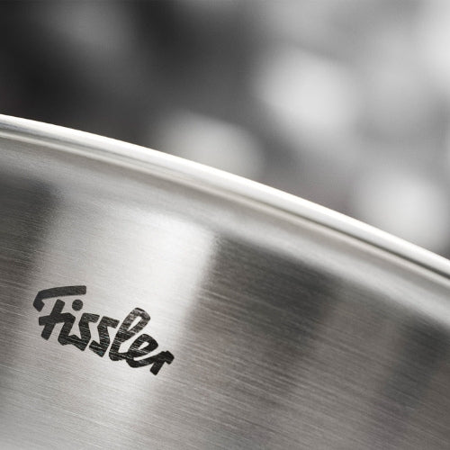 Detail eines Fissler-Edelstahltopfrandes, Logo auf gebürstetem Metall eingraviert - deutsches Präzisionskochgeschirr seit 1845, verschwommener grauer Hintergrund.