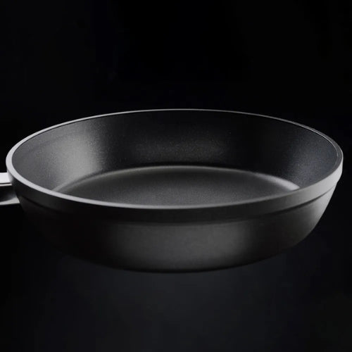 Schwarze antihaftbeschichtete Bratpfanne von Fissler mit ergonomischem Griff, der angewinkelt gezeigt wird, um die makellose, glatte Innenseite zu zeigen, die in Deutschland entwickelt wurde.