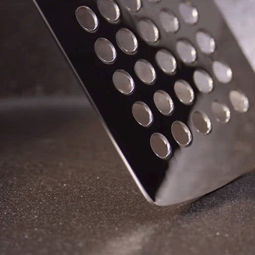Nahaufnahme einer Fissler-Edelstahlreibe mit Präzisionslochung, die vor einem dunklen, unscharfen Hintergrund leuchtet.