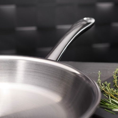 Fissler Edelstahlbratpfanne mit Präzisionsgriff auf dunkler Arbeitsplatte, daneben frische Kräuter, das typische deutsche Design im Fokus.
