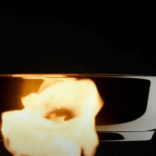 Eine Bratpfanne von Fissler aus rostfreiem Stahl stellt ihre Präzision und Langlebigkeit unter Beweis, während eine leuchtende Flamme vor einem dunklen Hintergrund aufsteigt.