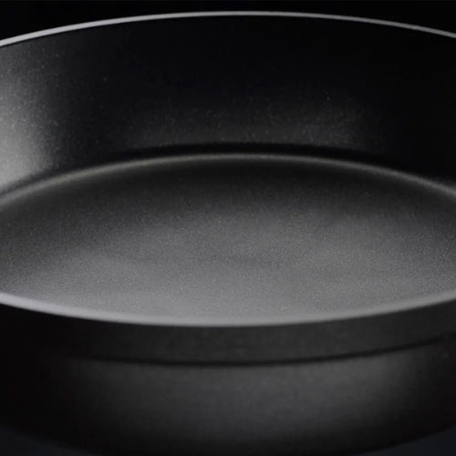 Eine Nahaufnahme einer in Deutschland hergestellten antihaftbeschichteten Bratpfanne von Fissler mit glatter Oberfläche und flachen Seiten auf dunklem Hintergrund.