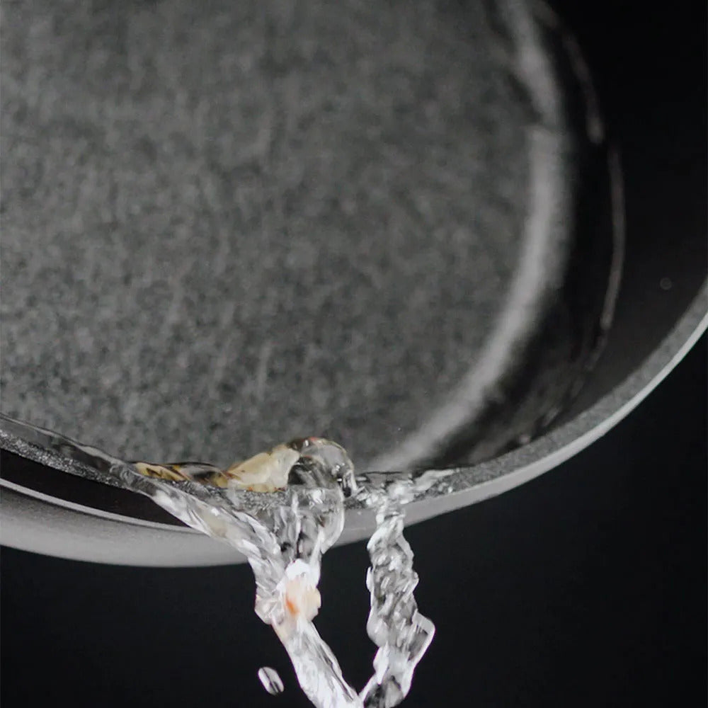 Aus einer Fissler Bratpfanne fließt das Wasser in Strömen. Präzise Technik und zeitloses deutsches Design auf schwarzem Hintergrund.
