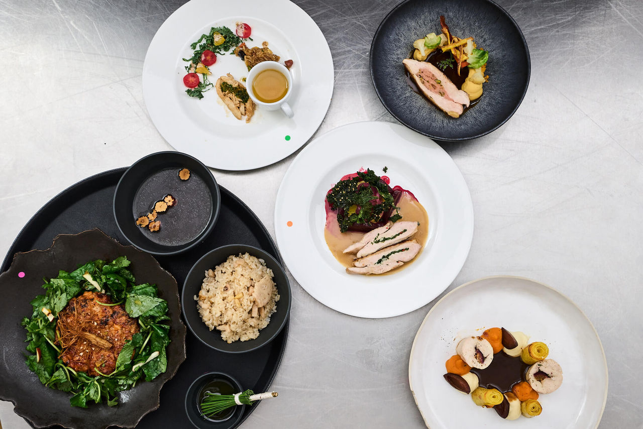 Five gourmet dishes with meat, vegetables, and sauces on Fissler stainless steel cookware in an elegant display.