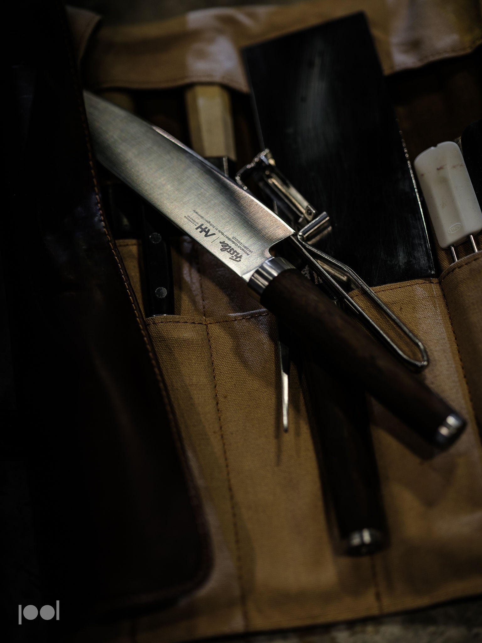 A precision-engineered Fissler chef’s knife with a dark handle is elegantly displayed on a tan knife roll, accompanied by premium kitchen tools and utensils that reflect German quality and timeless design.
